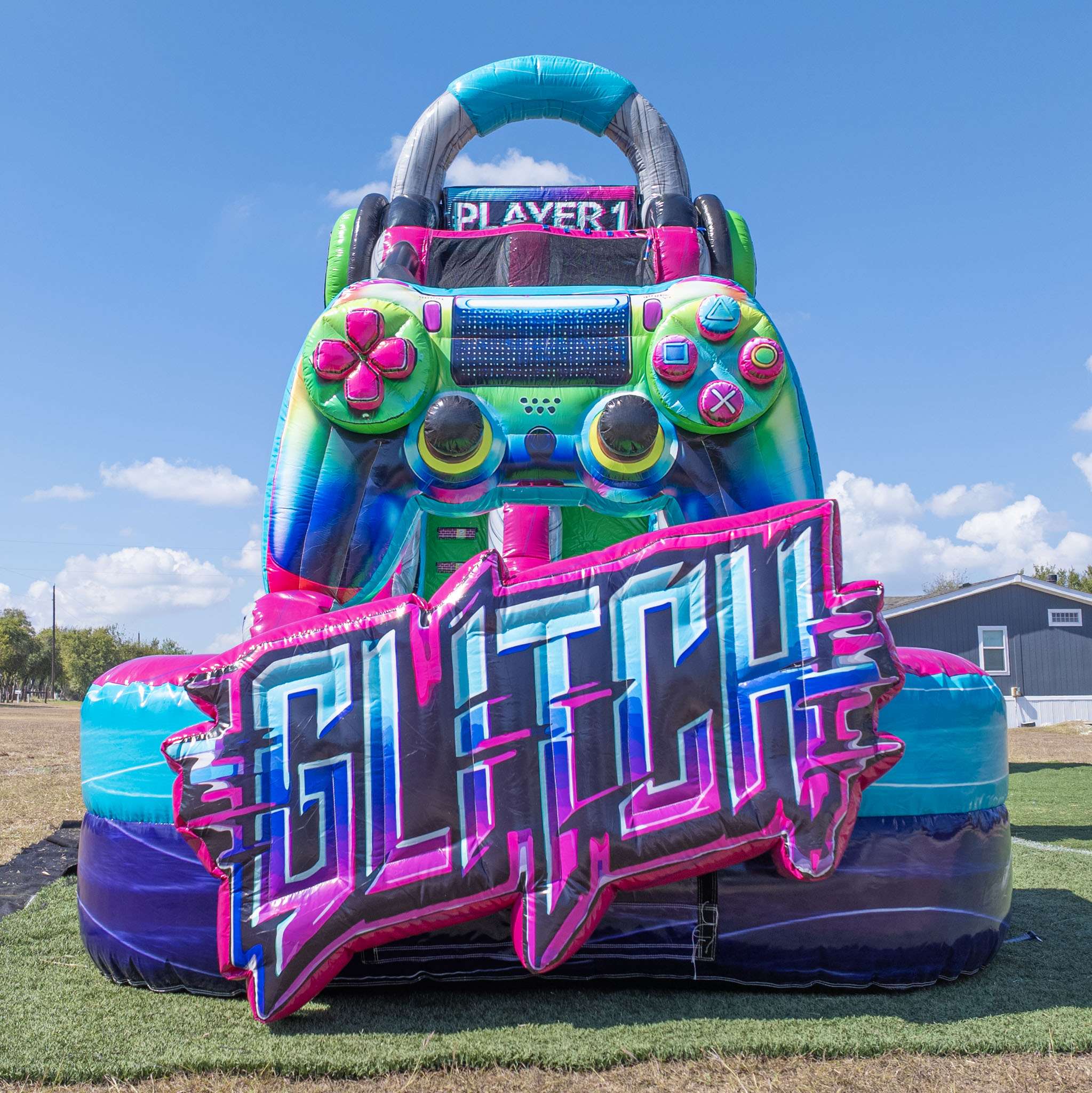 Tall pink green and purple Glitch gamer themed inflatable water slide standing in an open grassy yard under a blue sky