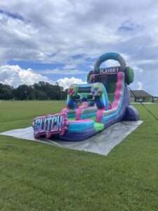 Tall teal and pink inflatable water slide set up on open grass under a wide Louisiana sky, showing the overhead clearance a big slide needs.