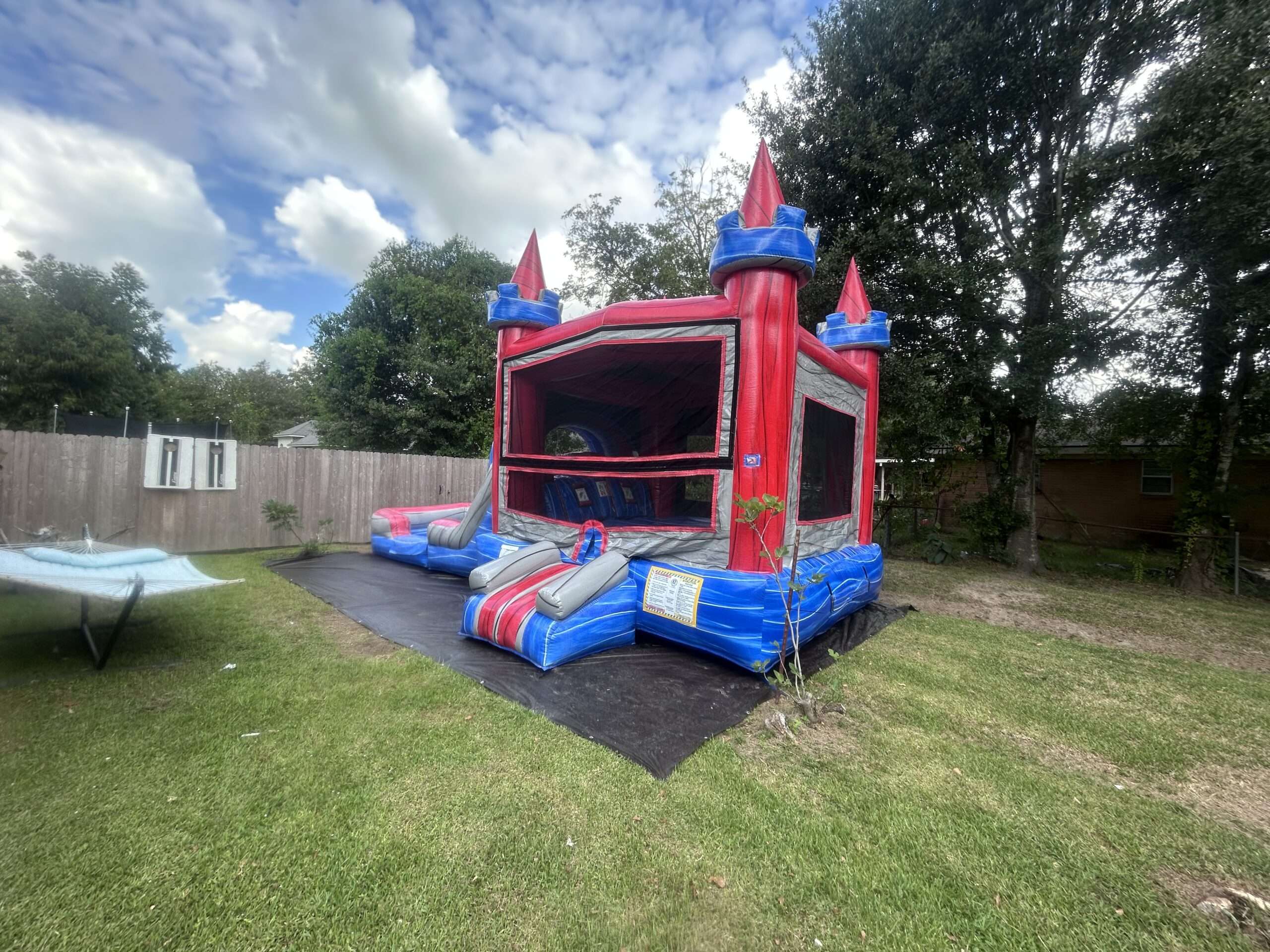 Red and blue castle bounce house combo with slide set up in an Acadiana backyard for a Thanksgiving family gathering