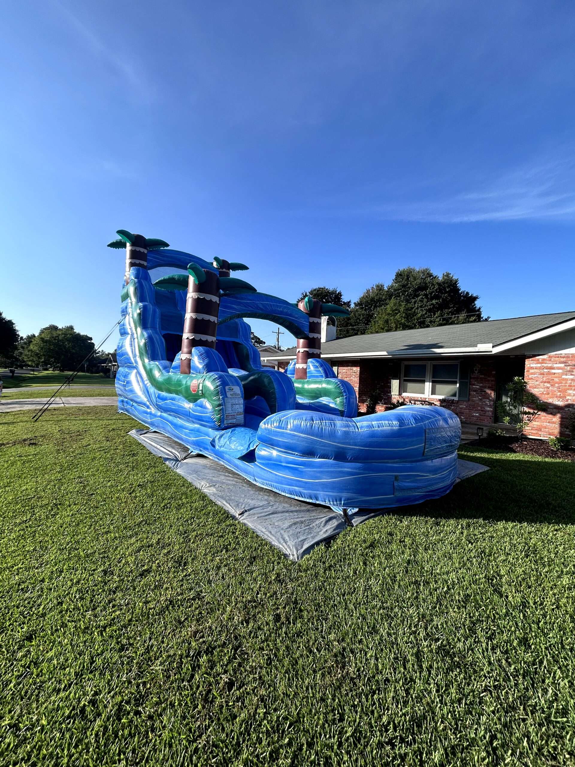 Blue tropical water slide with splash pool set up on a green front lawn in Youngsville, Louisiana under a clear October sky