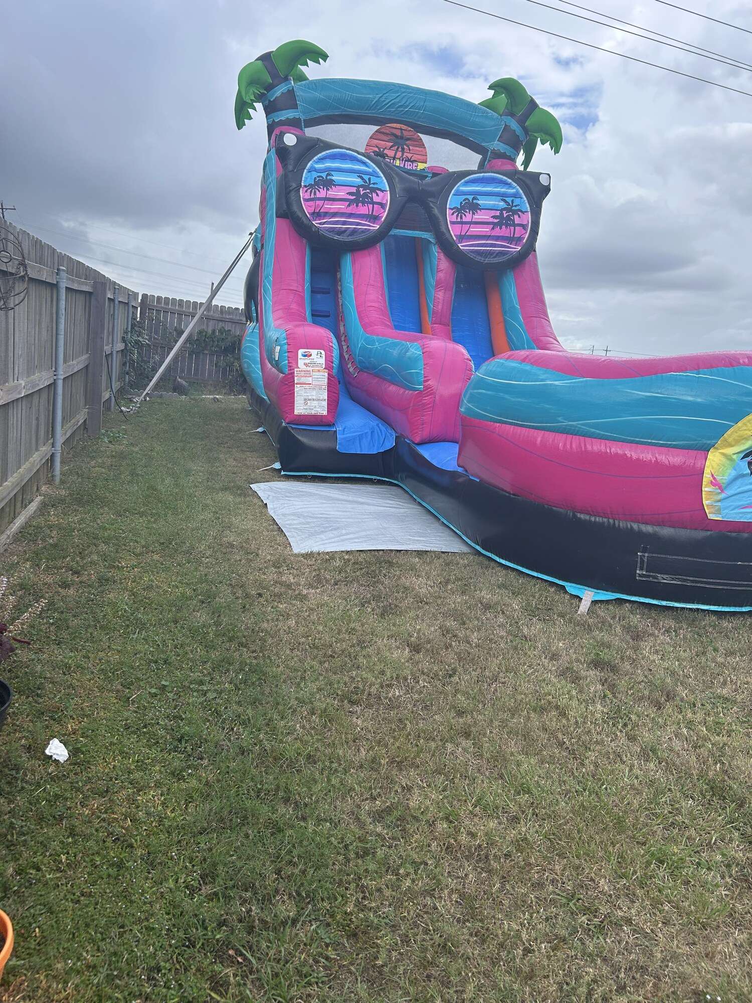 Tropical water slide rental anchored on a fenced side yard with a white ground tarp under the inflatable protecting the St. Augustine grass in Youngsville, LA