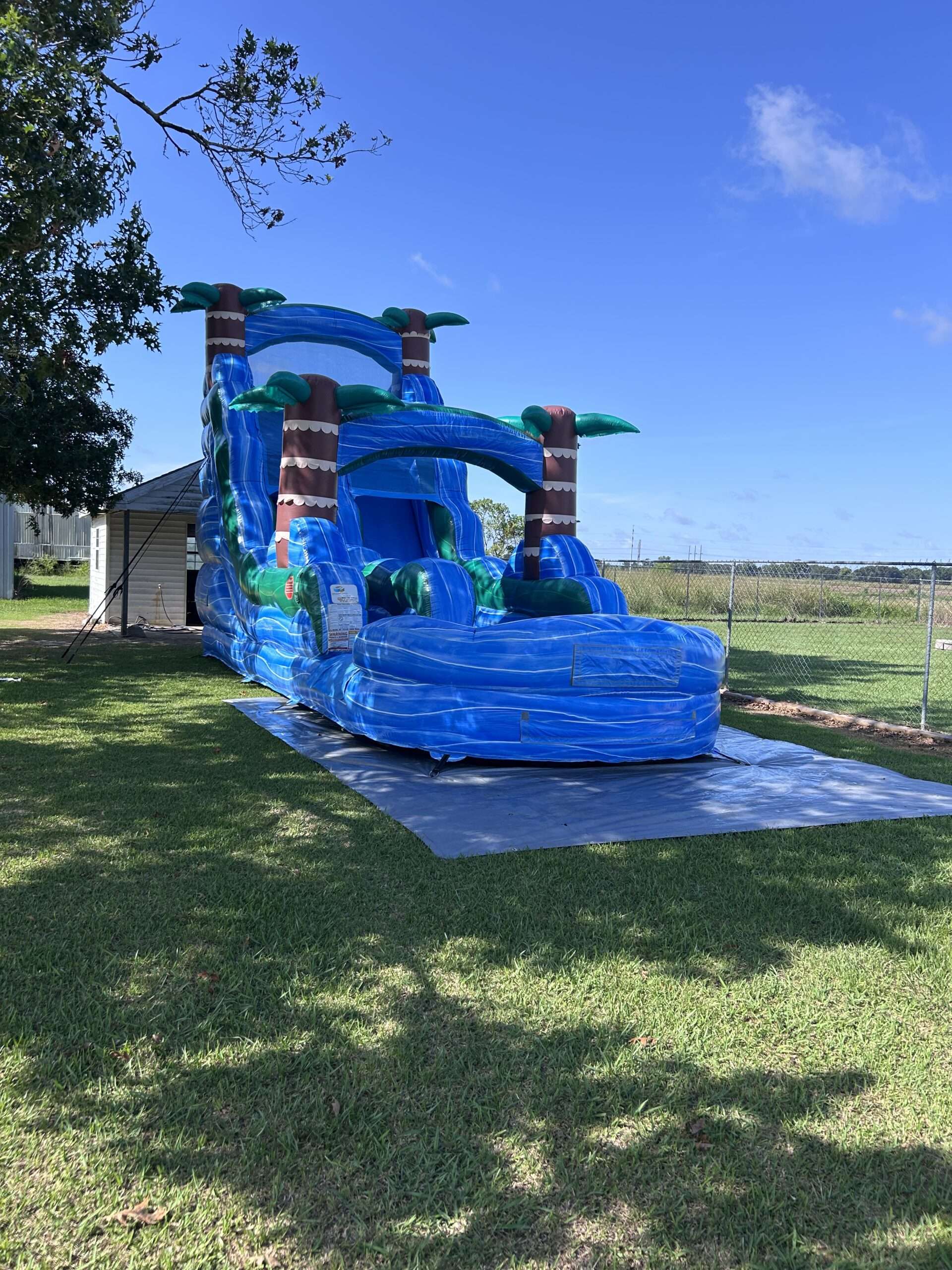 Blue palm-tree water slide inflatable set up on a grassy lawn for a Patriot Jumps party rental in Acadiana